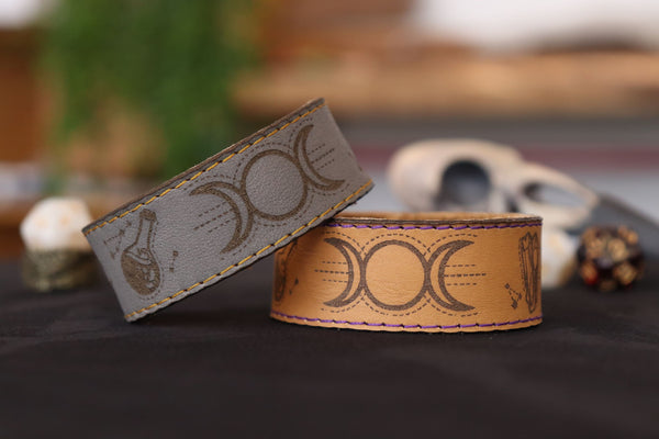 A grey leather bracelet with gold stitching and a brown leather bracelet with purple stitching
